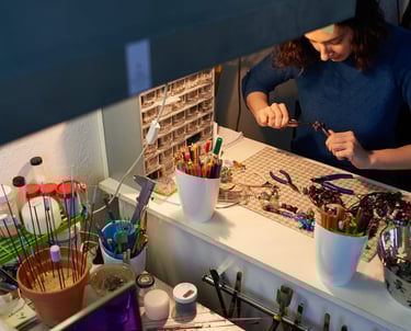 Mujer en un cuarto de taller de joyería manejando pinzas y piedras naturales 