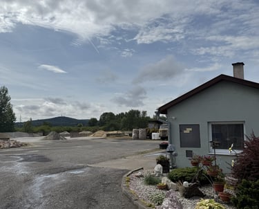 Areál VIZU Stavebniny vo Veľkých Kozmálovciach so skladovaným kamenivom, kanceláriou a okrasnou záhradkou.