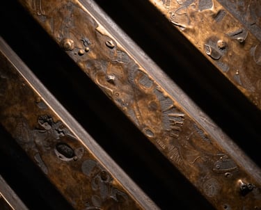 A close up of a bronze brown textured art piece with dramatic lighting from above, creating deep black shadows between the sculpted elements.