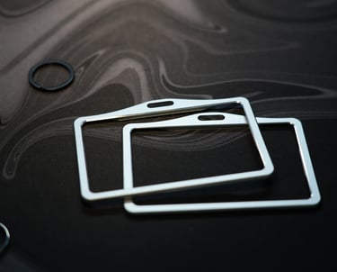 Two brushed metal ID badge holders on a dark marbled surface.