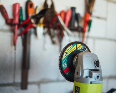A close-up of a Ryobi power tool, specifically a grinding machine, with various tools hanging on the wall in the background.