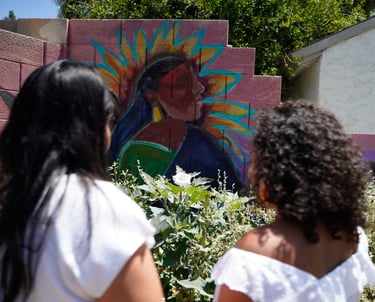 Iveth and Victoria standing in front of a Tonantzin's painting at the Giving Garden
