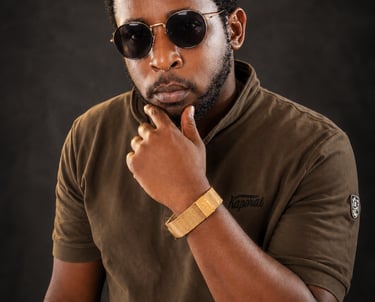 A stylish Ochomane wearing round sunglasses and a gold bracelet posing against a dark background.