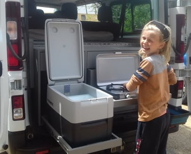 a young girl standing in front of a van with a coolerbox