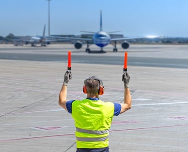a man in a yellow vest and safety vest holding a red light airplane marshall