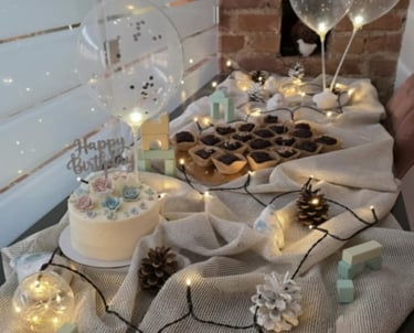Birthday cake with floral frosting and brownies on a table decorated with fairy lights and balloons.