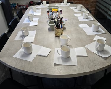 White ceramic mugs and paintbrushes on a table for a pottery painting workshop.