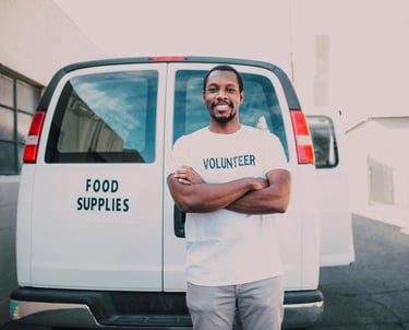 A male volunteer smiling and standing in front of a van with food donations