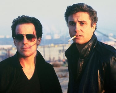 two men standing next to each other with a cigarette in the background