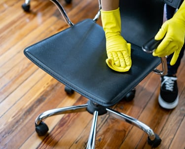Person cleaning a black office chair with yellow gloves.