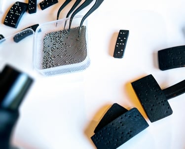 Fabrication de plaques en braille avec pinces, microbilles métalliques et supports noirs perforés.