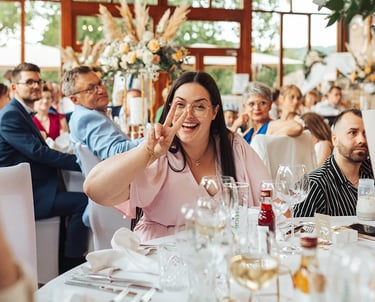 Invitée qui fait un signe de la main drôle alors qu'elle est à table durant un mariage.