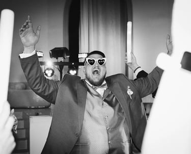 Le marié, lunettes de fête sur le nez, bras levés et sourire éclatant, profite de la soirée.