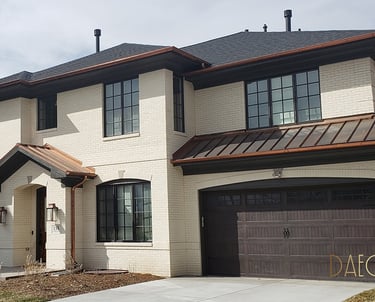 Two-story white brick home featuring copper gutters and a dark wood garage door.