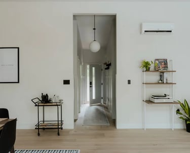 a room with a table and chairs and open front door looking down hall