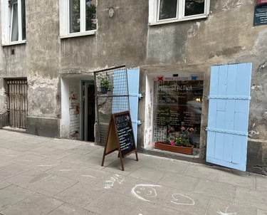 Manu Stalowa storefront in Warsaw with blue shutters and a chalkboard menu on a cobblestone sidewalk.