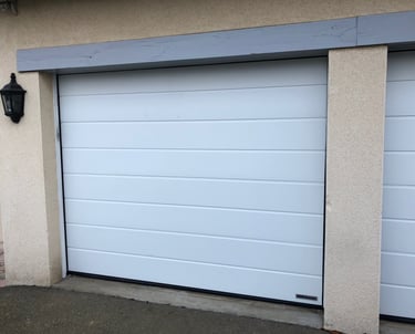 Porte de garage sectionnelle motorisée blanche à rainures horizontales installée en rénovation.