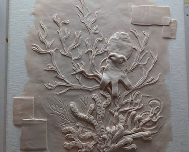 Layering elements and adding detail to a polymer clay relief sculpture on stretched canvas.