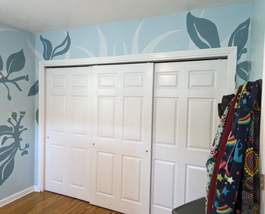 Painting colorful shapes on a wall mural surrounding closet doors.