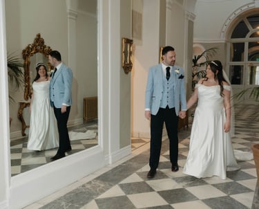 A bride and groom holding hands walking past a mirror in an elegant wedding lartington hall.