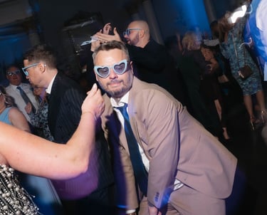 Wedding guests wearing fun heart-shaped sunglasses dancing at a relaxing evening reception party.
