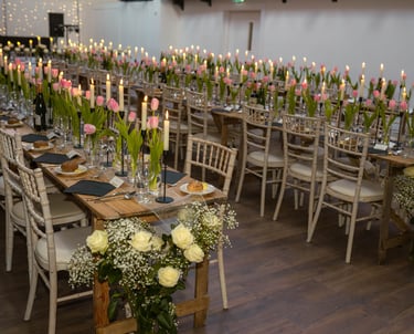 Wedding reception long wooden tables decorated with pink tulips, white roses, and lit candles.