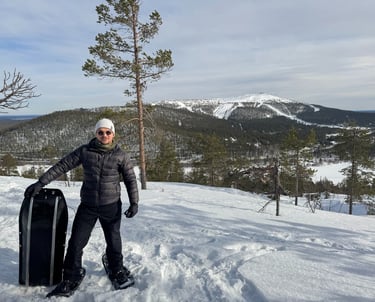 a man standing in the snow with a snowboard with a hill and beautiful snowy background