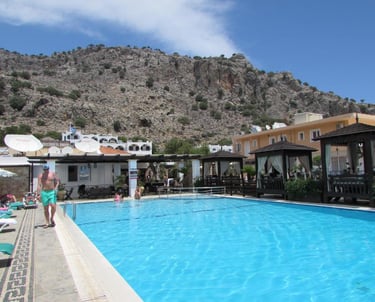 Luxury swimming pool at a Mediterranean resort with mountains and cabanas in the background.