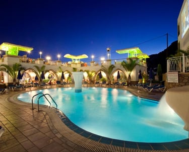 Illuminated outdoor resort swimming pool at night with lounge chairs and palm trees.