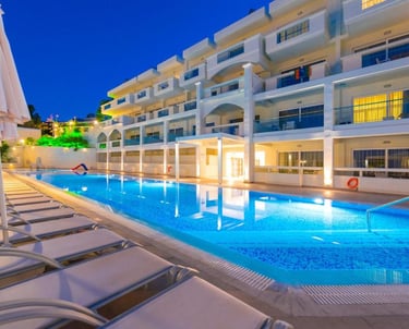 Luxury resort swimming pool illuminated at night with rows of sun loungers and hotel balconies.