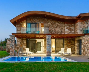 Luxury stone villa with a private swimming pool, wave-shaped roof, and lit patio at twilight.