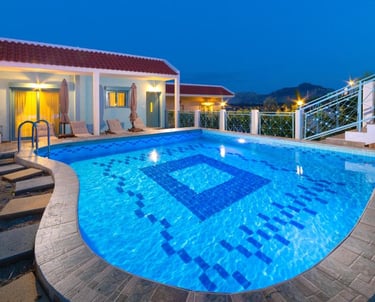 Luxury villa rental with a lit private swimming pool and red tile roof at twilight.
