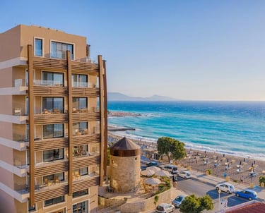 Luxury beach hotel overlooking the turquoise Mediterranean Sea and a historic stone windmill in Rhodes, Greece.