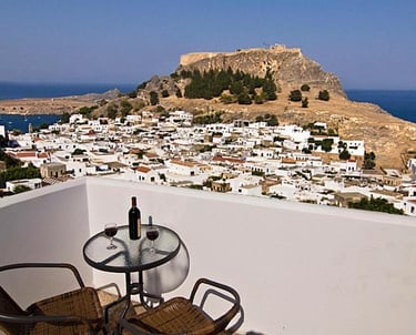 Wine on a balcony overlooking the Lindos Acropolis and whitewashed village in Rhodes, Greece.