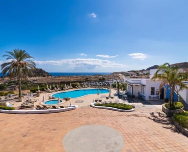 Luxury resort pool area overlooking the ocean in Rhodes, Greece with palm trees and sun loungers.