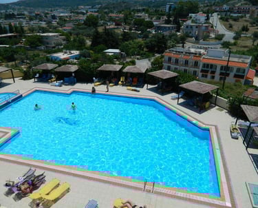 Aerial view of a bright blue swimming pool at a Mediterranean hotel resort with sun loungers and cabanas.