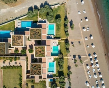 Aerial view of a luxury beachfront resort with private pools and white umbrellas on a sandy shore.