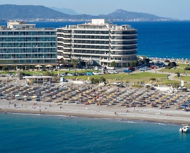 Aerial view of a beach resort in Rhodes, Greece, with waterfront hotels and sun loungers on the sand.