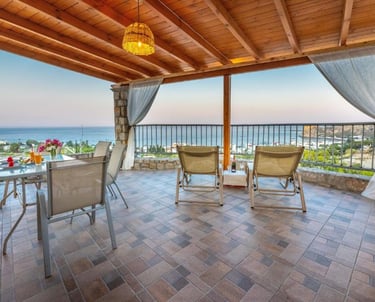 Luxury villa terrace with ocean views, outdoor dining table, and lounge chairs under a wooden pergola.