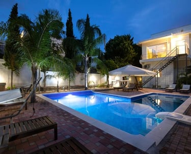 Luxury villa backyard with a lit swimming pool, palm trees, and lounge chairs at twilight.
