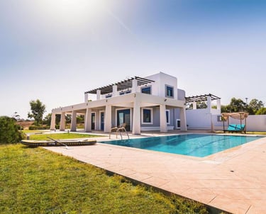 Luxury white villa with private swimming pool, sun lounge area, and green lawn under a clear sky.