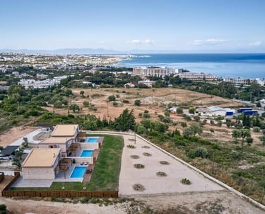 Aerial view of luxury holiday villas with private pools near the coastal shoreline in Greece.