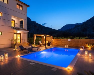 Luxury villa with an illuminated swimming pool and outdoor lounge at twilight in the mountains.