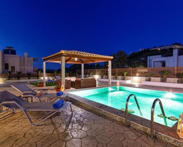 Luxury villa patio with illuminated swimming pool, lounge chairs, and a covered gazebo at night.