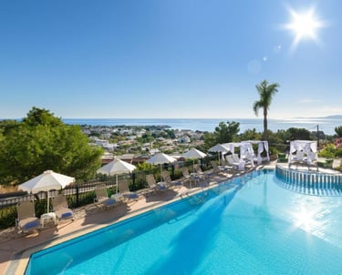 Luxury hotel swimming pool with sun loungers and ocean views under a bright sunny sky.