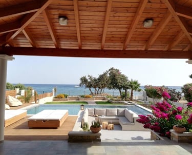 Luxury beachfront villa patio with a swimming pool, sunken lounge, and ocean view under a wood pergola.