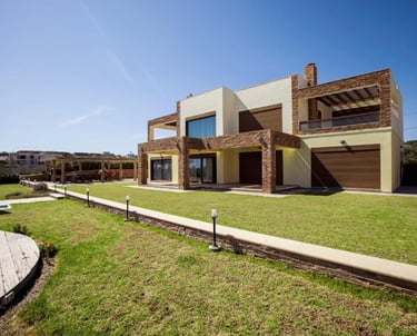 Modern luxury villa with a manicured green lawn and stone architectural details under a blue sky.