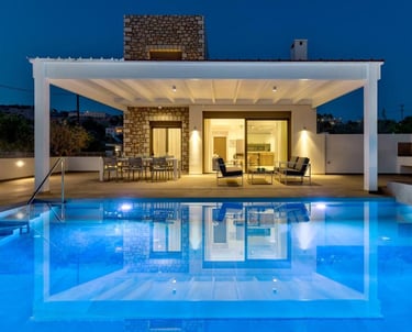 Luxury modern stone villa with a blue swimming pool and lit patio at night.
