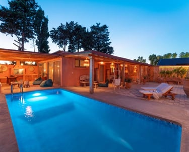 Luxury private villa with a glowing swimming pool, patio furniture, and rustic outdoor lounge at dusk.