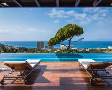 Luxury infinity pool with sun loungers on a wooden deck overlooking the blue ocean and resort skyline.